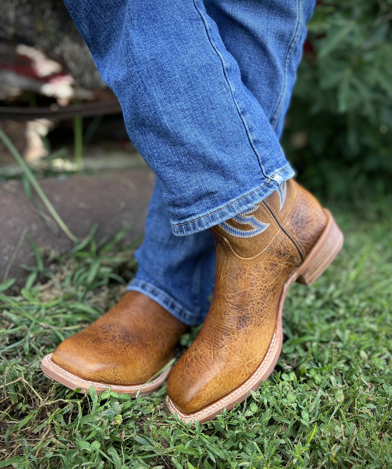 A man standing in grass with his cowboy boots 