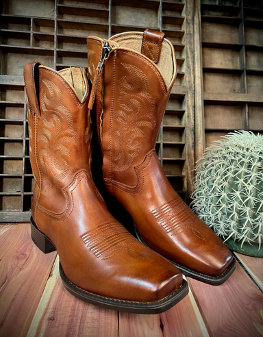 Pair of brown cowboy boots on a wooden surface with a cactus in the background
