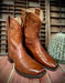 Pair of brown cowboy boots on a wooden surface with a cactus in the background