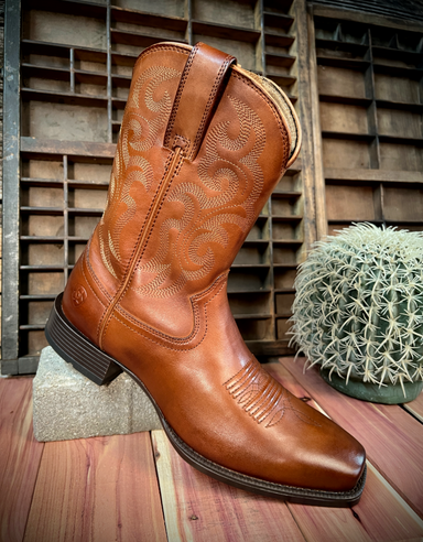 Brown cowboy boot on a wooden surface with a rustic background