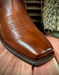 Brown leather boot with detailed stitching on a wooden surface