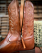 Close-up of a brown leather boot shaft with intricate western stitching and a zipper.