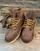 Pair of brown leather boots with yellow laces on a wooden surface, featuring the Danner brand.