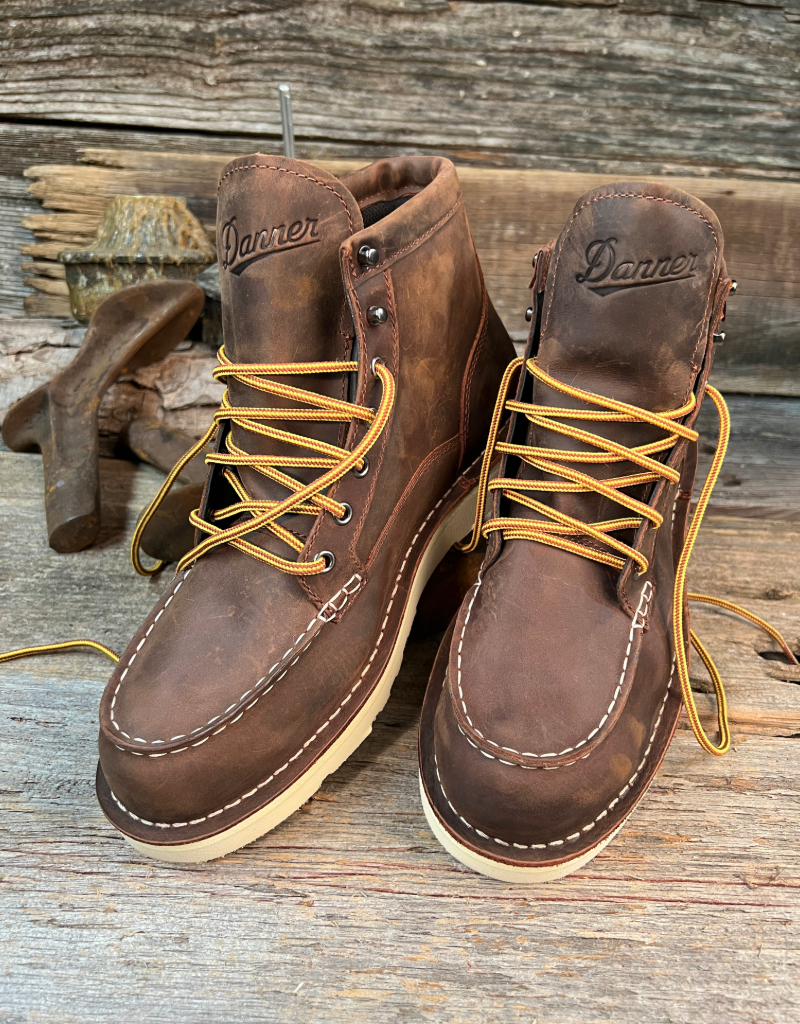 Pair of brown leather boots with yellow laces on a wooden surface, featuring the Danner brand.