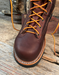 Brown leather boot with orange laces on a wooden surface
