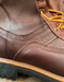 Close-up of a brown leather boot with orange laces on a wooden surface