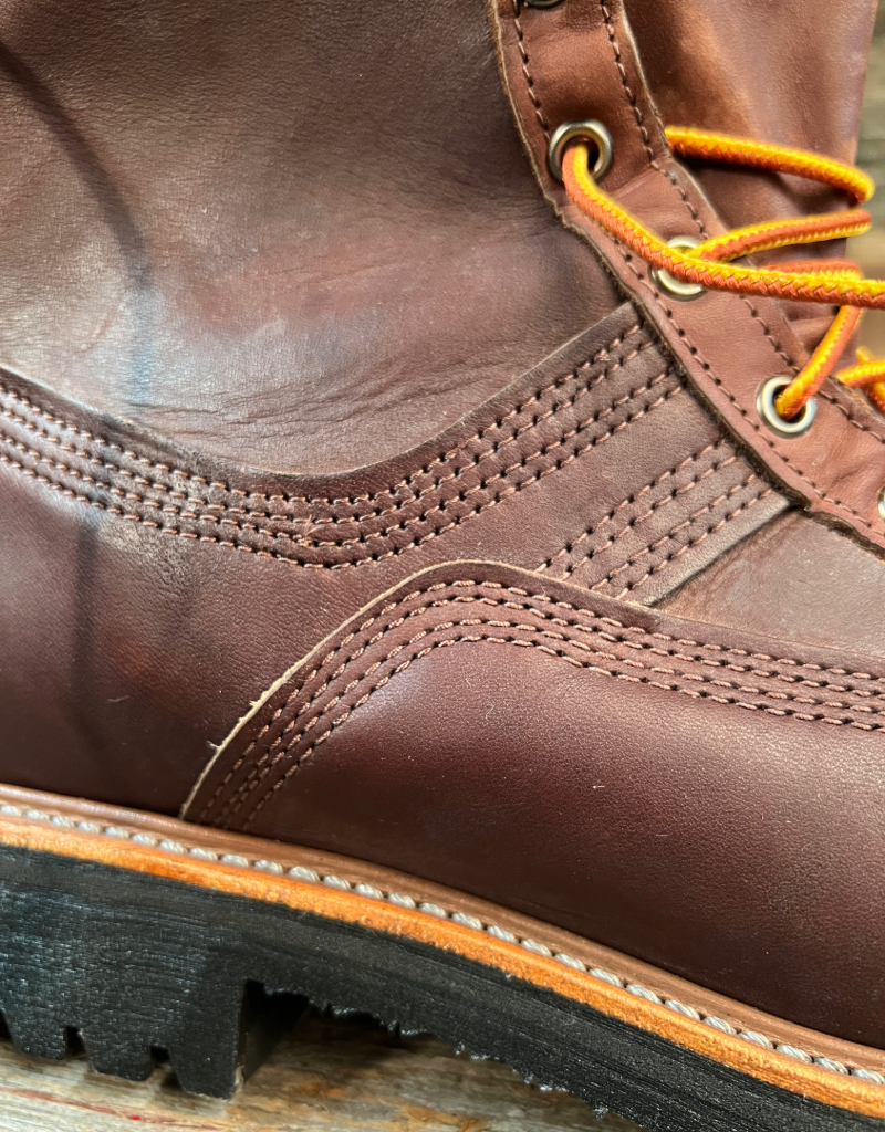 Close-up of a brown leather boot with orange laces on a wooden surface