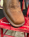 Brown leather boot with intricate stitching on a red chair