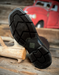 Close-up of a black boot sole on a wooden surface with a red vehicle in the background.