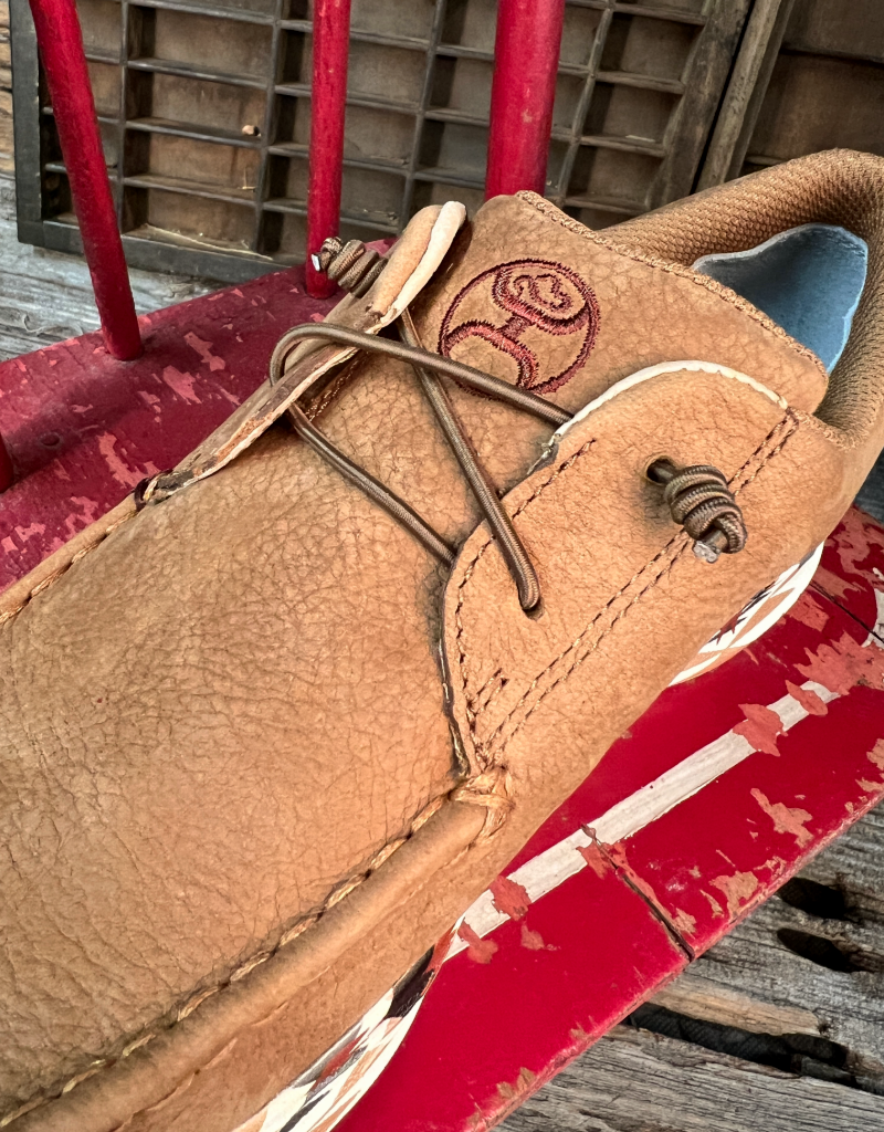 Close-up of a brown leather shoe with a Hooey brand logo and elastic laces on a red surface.