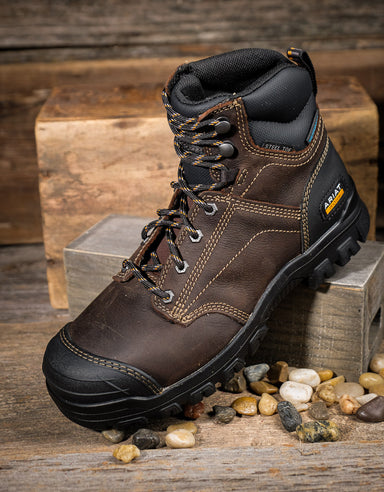 Brown leather boot with black sole on a wooden surface with pebbles