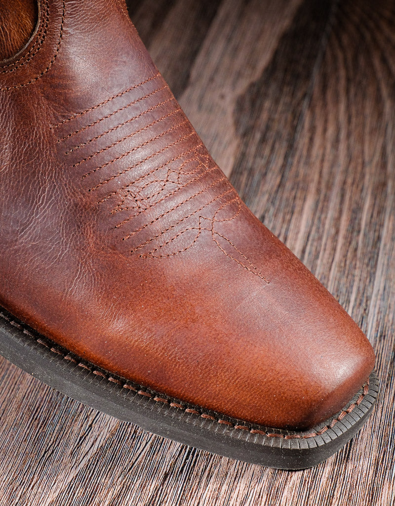 A narrow square toe on a brown boot with a wooden background