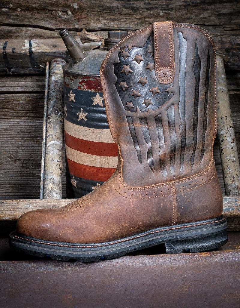 A single pull on boot with a stamped star and stripes pattern in the top leather shaft and a background of wood
