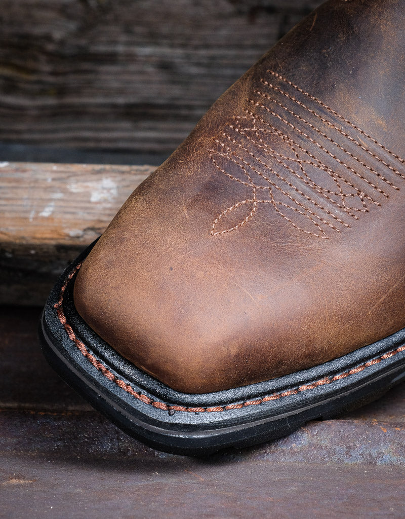 Close up on square toe brown western boot toe with a blurred wooden background