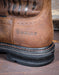 Closeup of western heel with the Ariat logo stamped into the leather. The heel is black and resting on a metal sheet