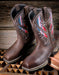 Pair of brown cowgirl boots with colorful vent panels on a wooden surface