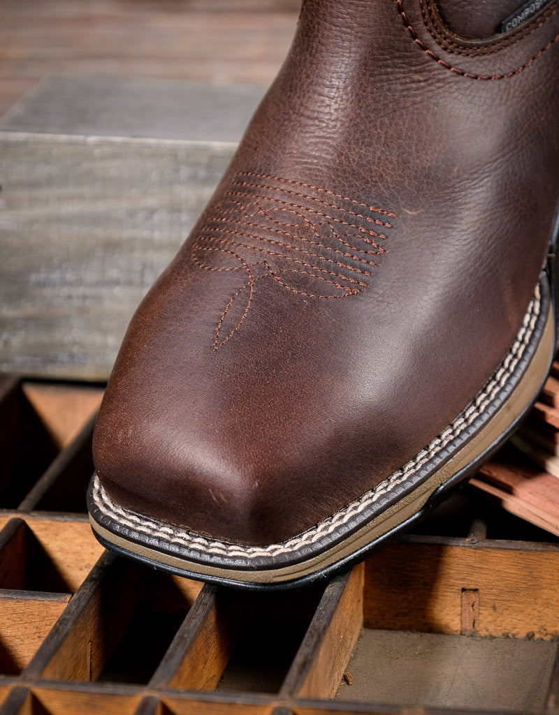 Brown leather boot with detailed stitching on a wooden surface