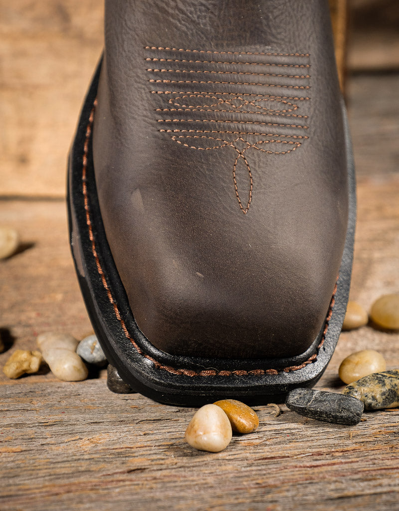 Close-up of a brown leather boot square toe with stitching detail on a wooden surface with stones.