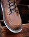 Brown leather boot with laces on a wooden surface, featuring the Ariat logo.