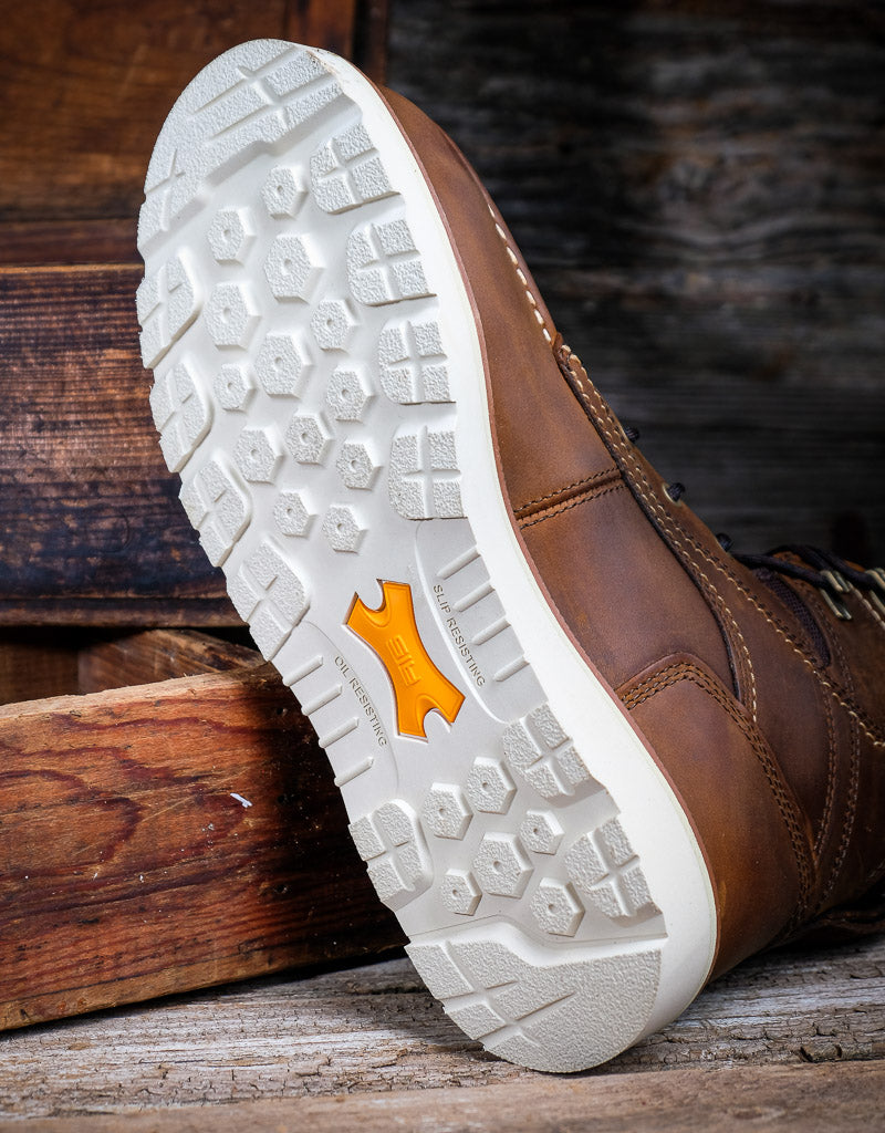 Brown leather shoe with white sole and orange logo on a wooden surface