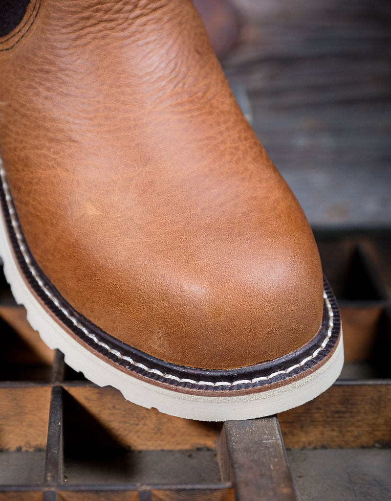 Close-up of a brown leather boot toe with a white sole on a wooden surface