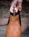 Brown leather boot with a hand holding the boot loop pull tab on the front of the boot