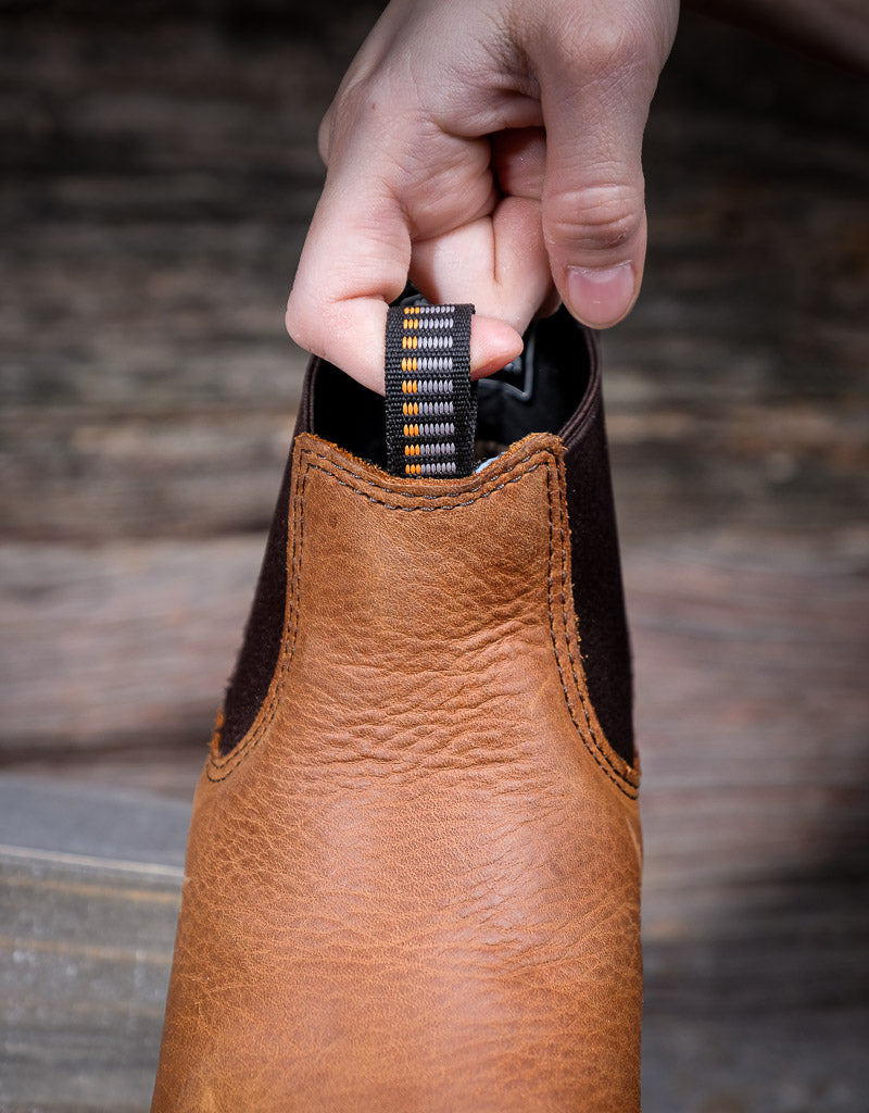 Brown leather boot with a hand holding the boot loop pull tab on the front of the boot