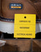Brown work boot with Ariat label and a yellow tag indicating features like composite toe, waterproof, and electrical hazard protection.
