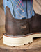 Brown leather boot with blue shaft on a wooden surface, featuring the Ariat logo.