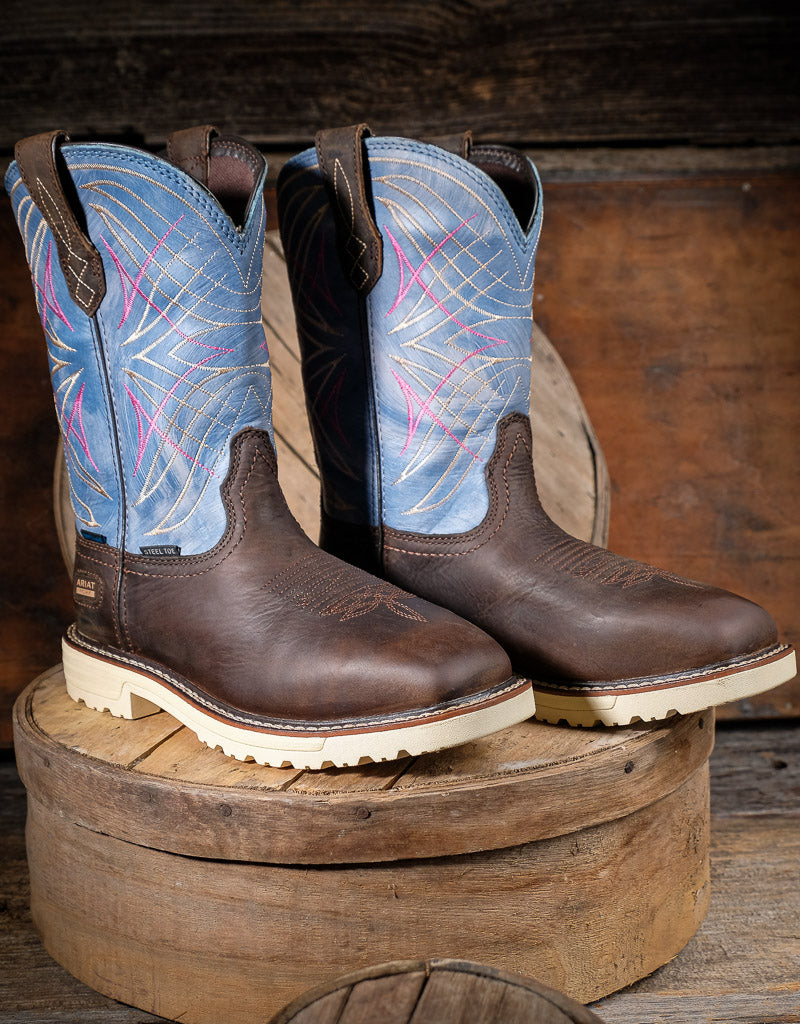 Pair of brown cowboy boots with blue and pink stitched tops on a wooden block.