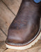 Close-up of a brown leather boot with white sole on a wooden surface