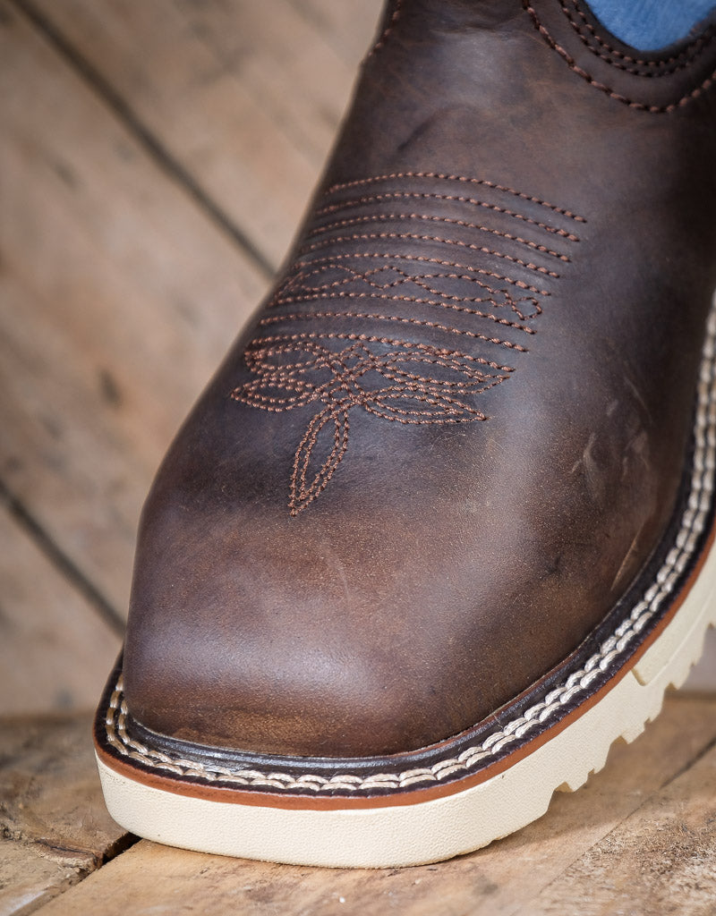 Close-up of a brown leather boot with white sole on a wooden surface