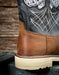 Close-up of a boot with detailed stitching and leather finish against a wooden background