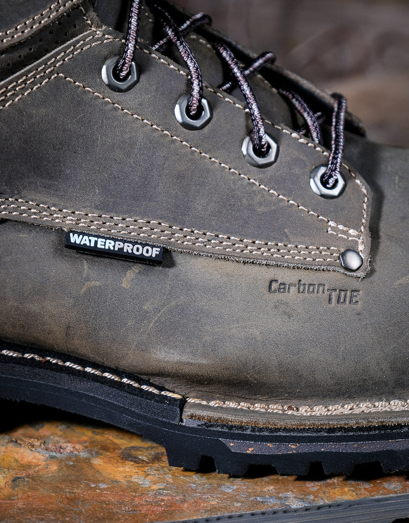 Close-up of a grey leather boot with 'Waterproof' label on a rustic surface