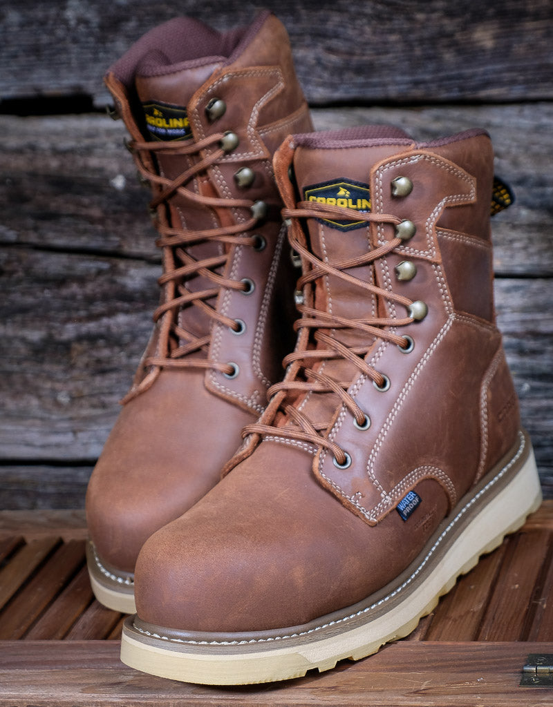 Pair of brown leather boots with visible Carolina brand logo on a wooden background