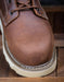Close-up of a brown leather boot with white sole on a wooden floor.