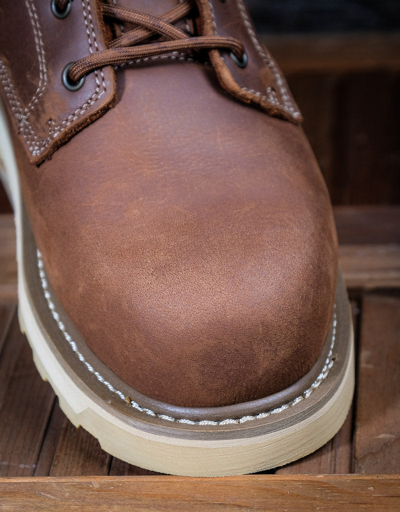 Close-up of a brown leather boot with white sole on a wooden floor.