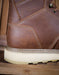 Close-up of a brown leather boot with white sole on a wooden surface