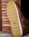 Close-up of a brown leather shoe with a textured sole on a wooden surface.
