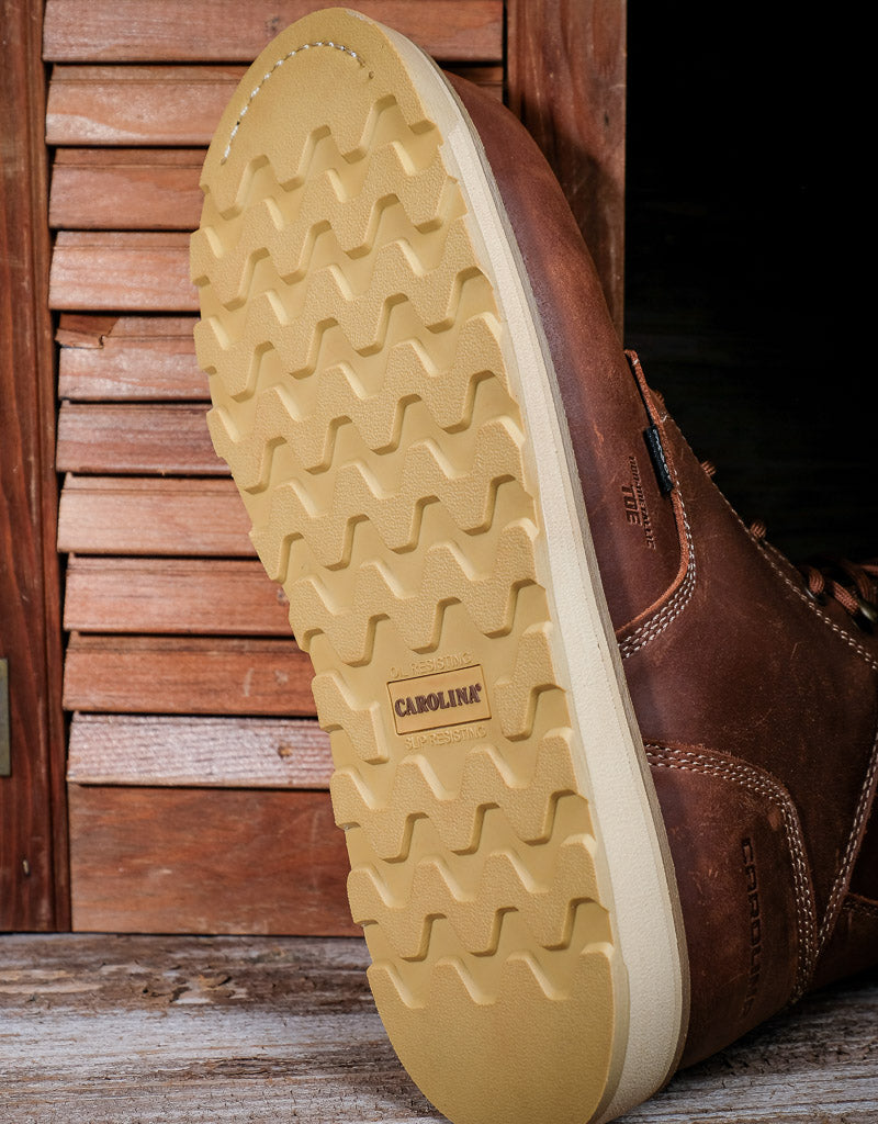 Close-up of a brown leather shoe with a textured sole on a wooden surface.