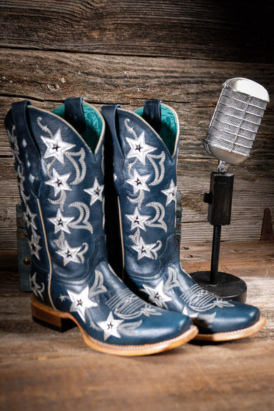 Blue cowgirl boots with star patterns on a wooden surface with a vintage microphone.