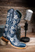 Blue cowgirl boot with star patterns on a wooden surface with a microphone in the background.
