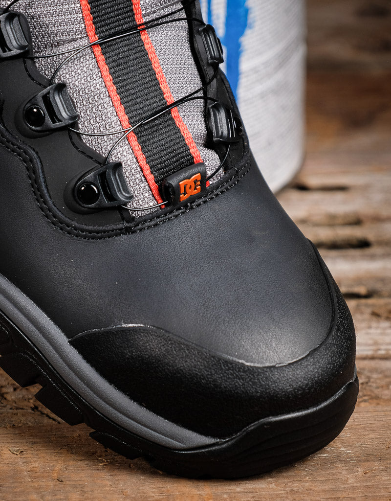 Close-up of a black and gray DC hiking boot with orange accents, resting on a rustic wooden surface.