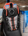A close-up of a black DC boot with gray mesh panels, bright orange accents, and a BOA dial closure, positioned next to paint cans on a rustic wooden surface.