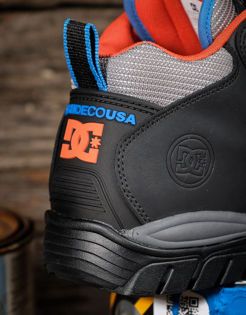 Close-up of a DC Shoes DC USA sneaker in black, gray, orange, and blue, showing the heel, DC logo, and pull tabs.