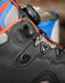 Close-up of a black high-top shoe with a dial closure system, featuring gray mesh panels, orange stitching, and blue accents.