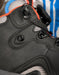 Close-up of a black high-top shoe with a dial closure system, gray mesh panels, and bright orange and blue accents.