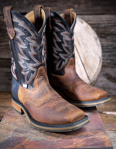 Pair of brown and black cowboy boots on a wooden surface with a rustic background.