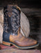 Brown and black cowboy boot with intricate western design on a wooden background