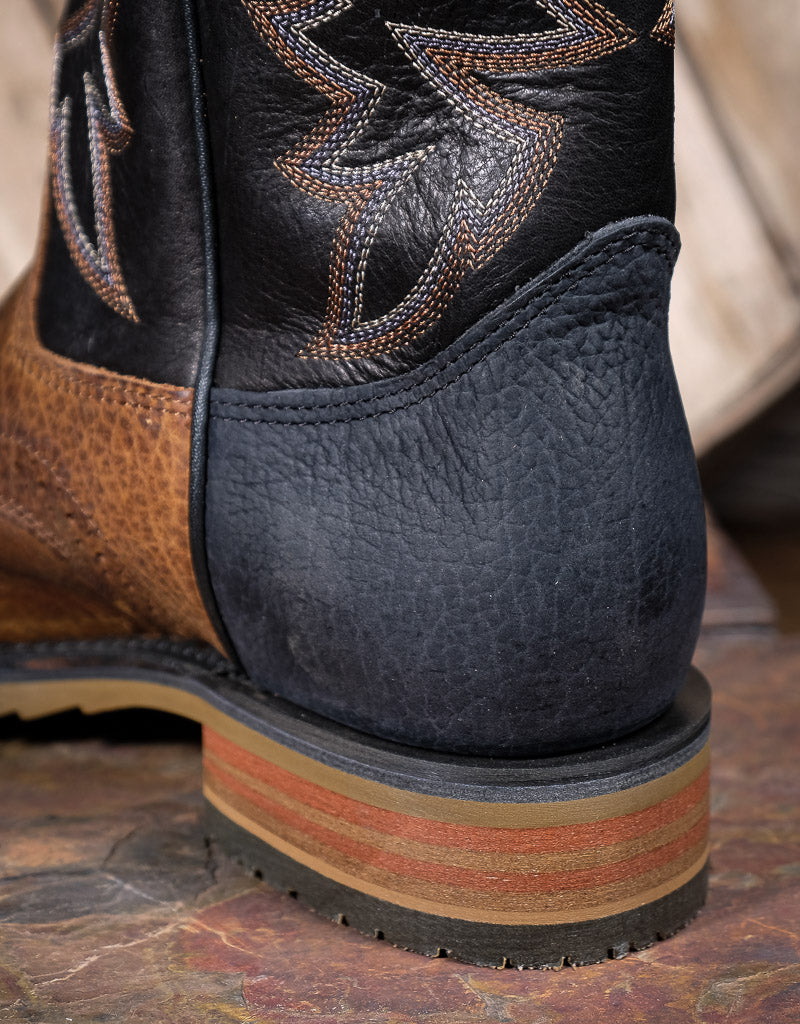 Close-up of a black leather boot heel with brown stacked heel base on a wooden surface